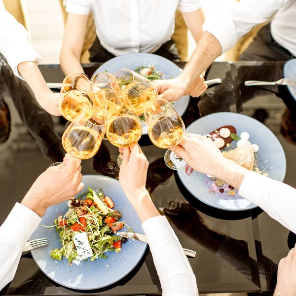 Business people clinking with wine glasses during a lunch with delicious meals at the restaurant, top view