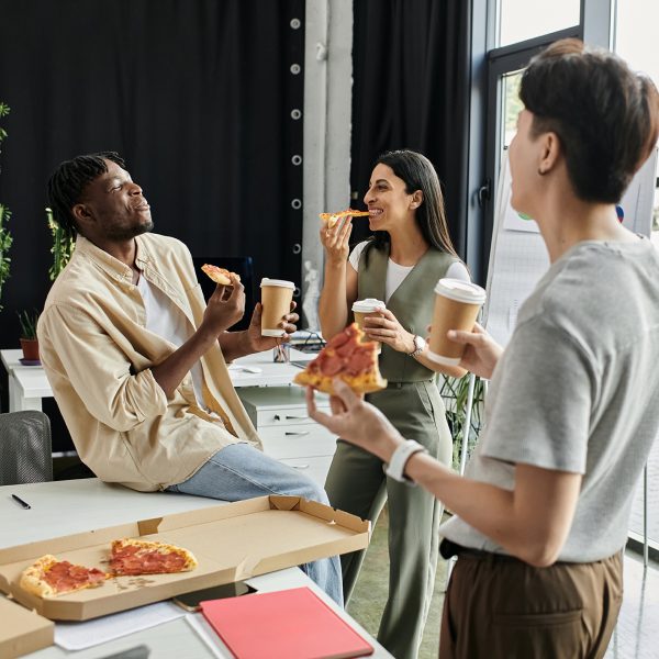 A group of four colleagues take a break from work, enjoying pizza and coffee together.