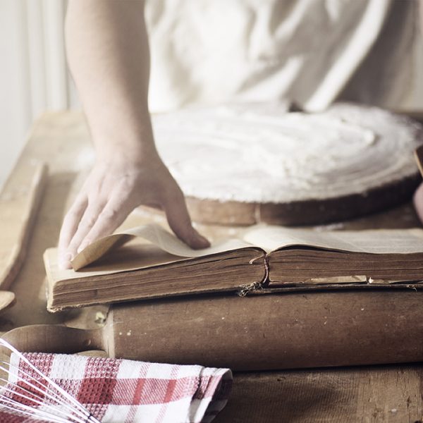Man preparing traditional recipe from vintage cookbook. Chef baking homemade dough on the kitchen table.