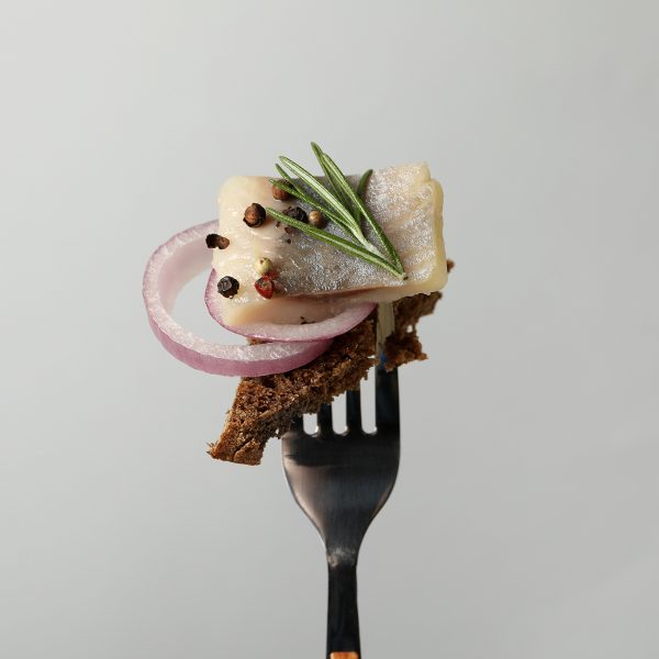 Fork with herring fish, bread and spices on light gray background